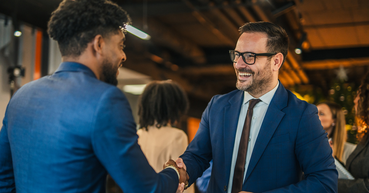 Two gentlemen shaking hands during a networking event, to illustrate the relationships that can be built at the PR and Comms Summit.