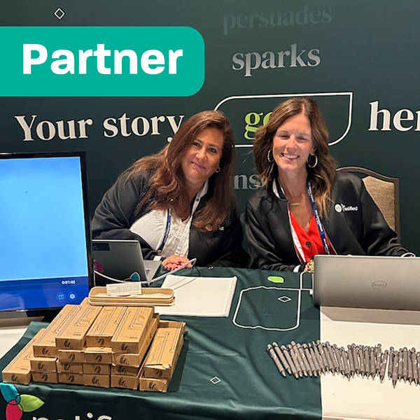 Two women lean in and smile while working a sponsorship table for Notified during a past PR & Comms Summit.