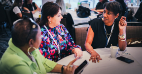 Three ladies sit at a round table during a past PR & Comms Summit deep in conversation.