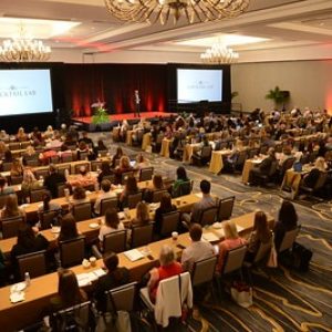 Virtual conference recorded general sessions, seated FPRA members looking at a presenter flanked by giant screens